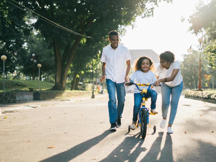 woman and man teaching little girl how to ride a bike