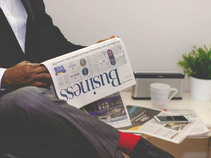 man holding and reading a newspaper that says "Business"