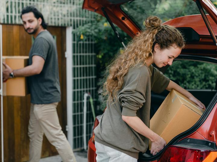 two people moving and a woman putting a moving box in the car