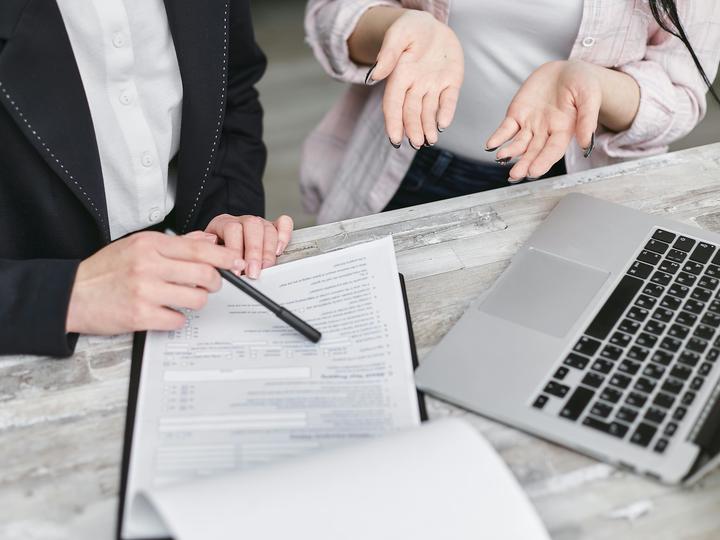 man holding a pen and woman talking with her hands with a computer on the table