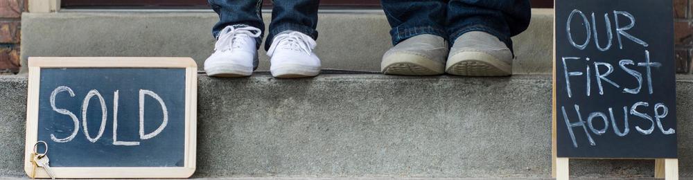 two sets of feet on steps with signs that say "sold" and "our first house"